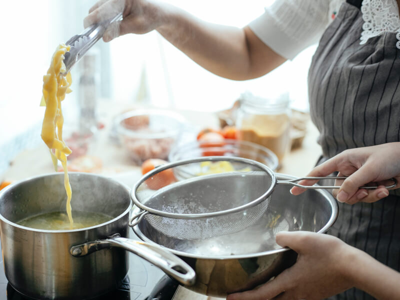 A person retrieves there cooked homemade pasta from a pot.